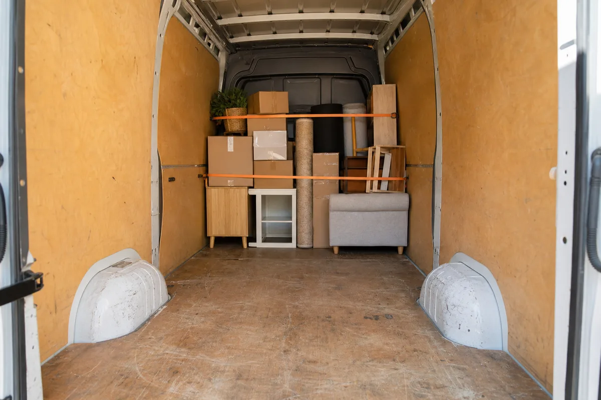 Intérieur d&rsquo;un camion de déménagement à moitié chargé, meubles sanglés contre la paroi avant, lumière naturelle