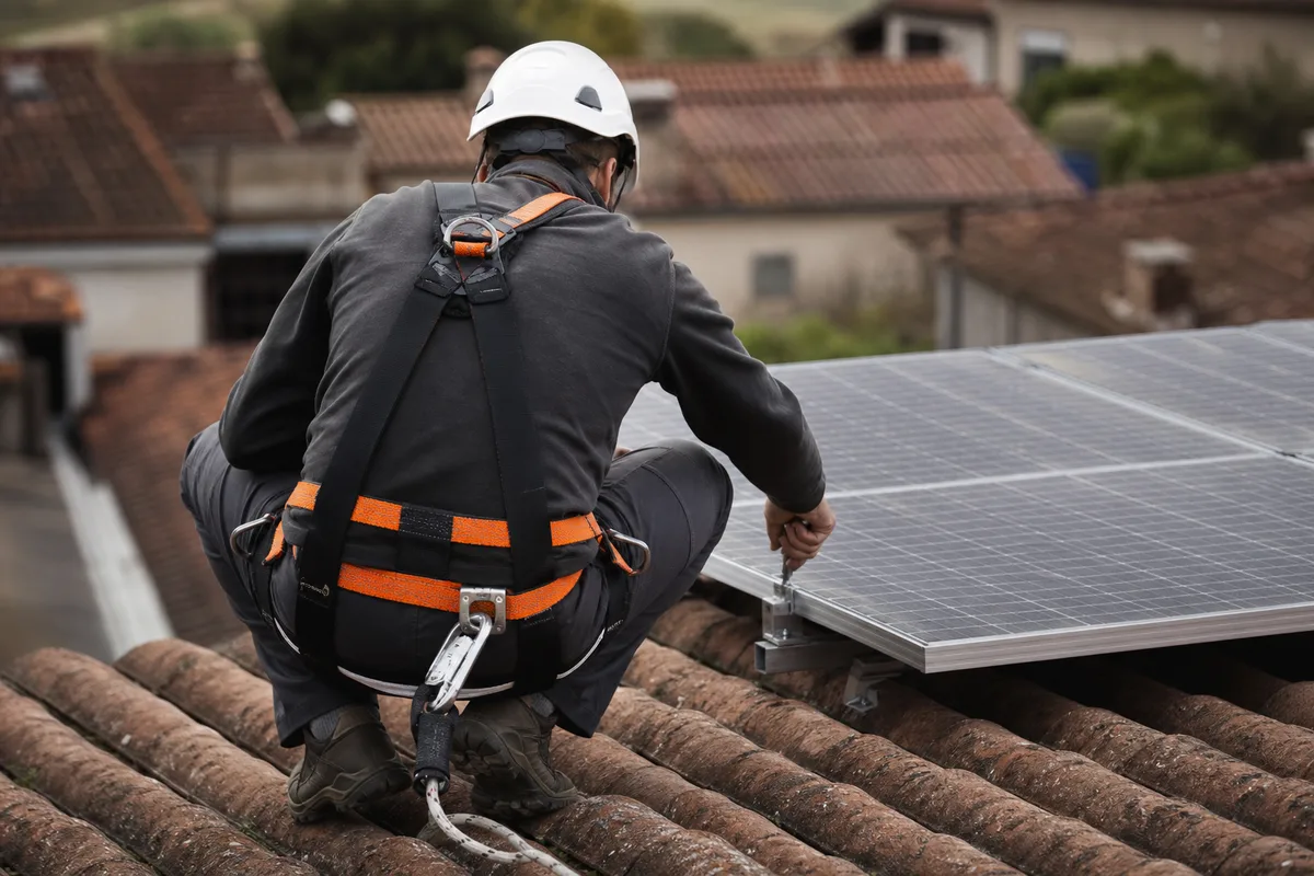 Technicien de dos en train de vérifier des panneaux solaires sur une toiture en tuiles